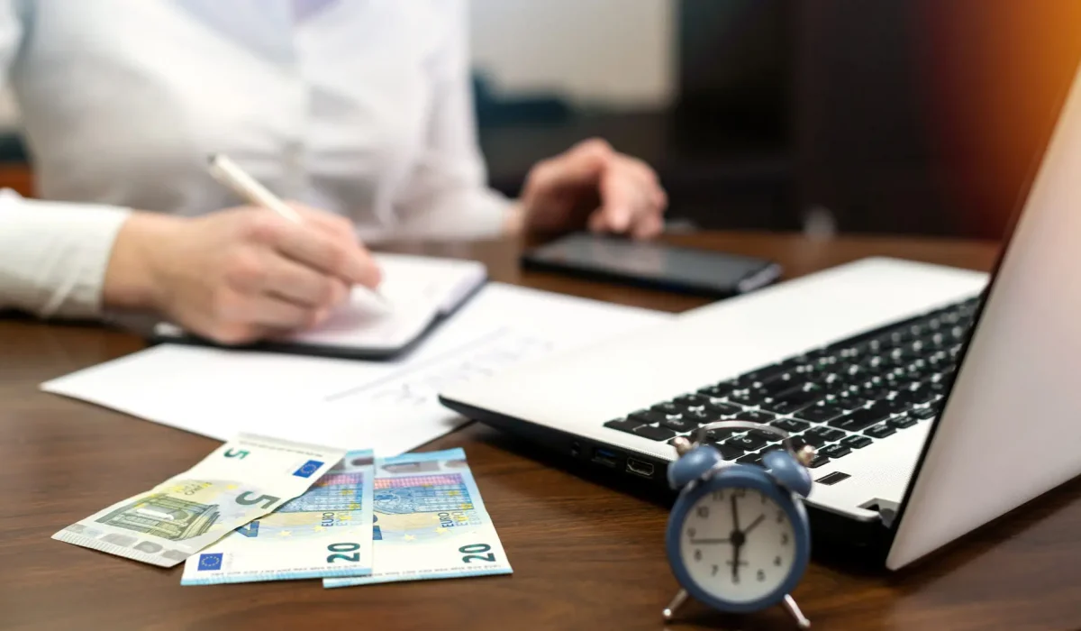 Woman working with finances on the table. Laptop, smartphone, money, notepad, clock